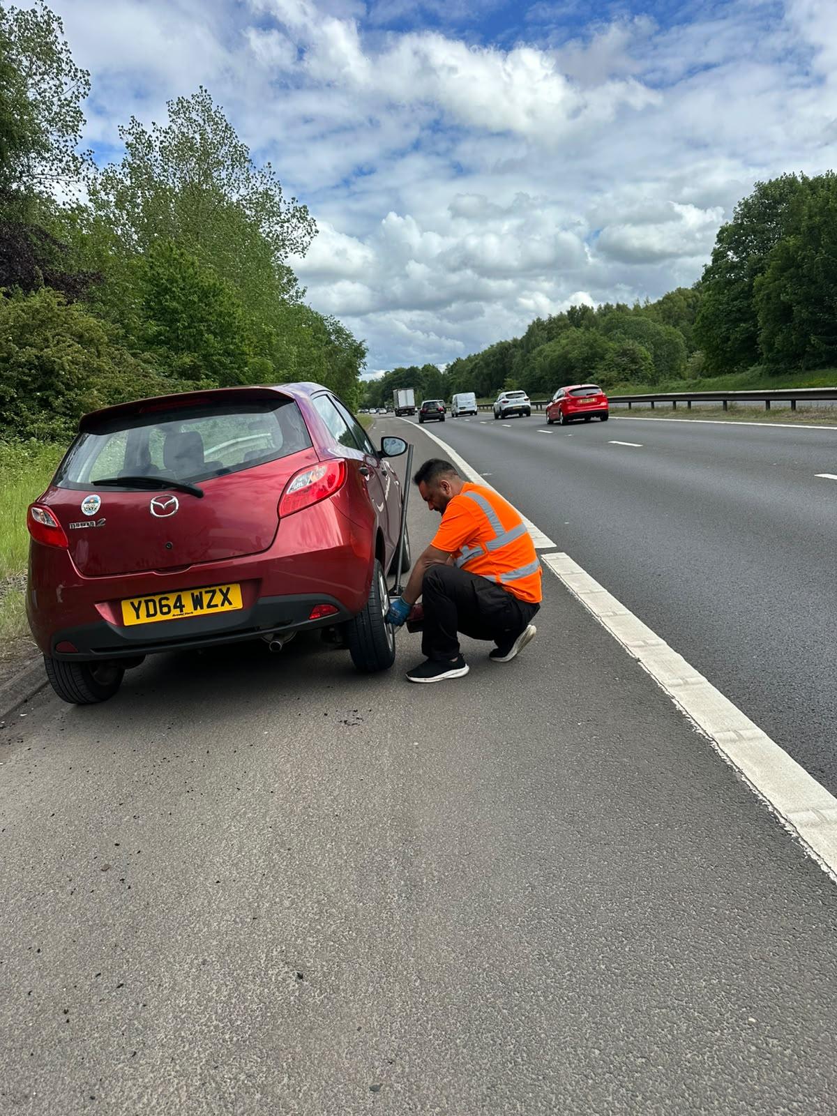 Mobile tyre fitter replacing a wheel beside a motorway